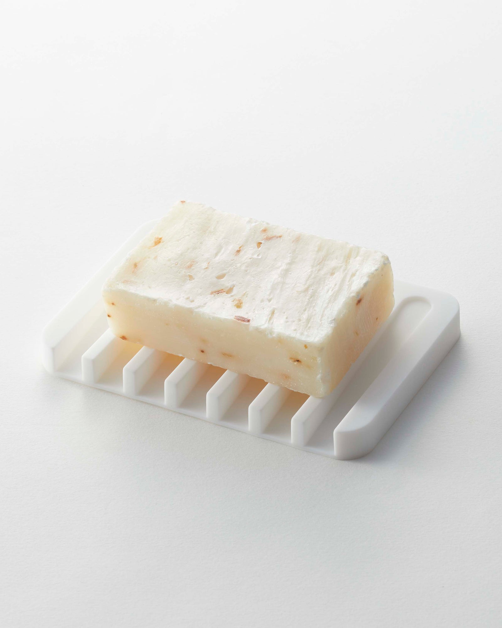 Bar of soap on a white soap dish against a light gray background
