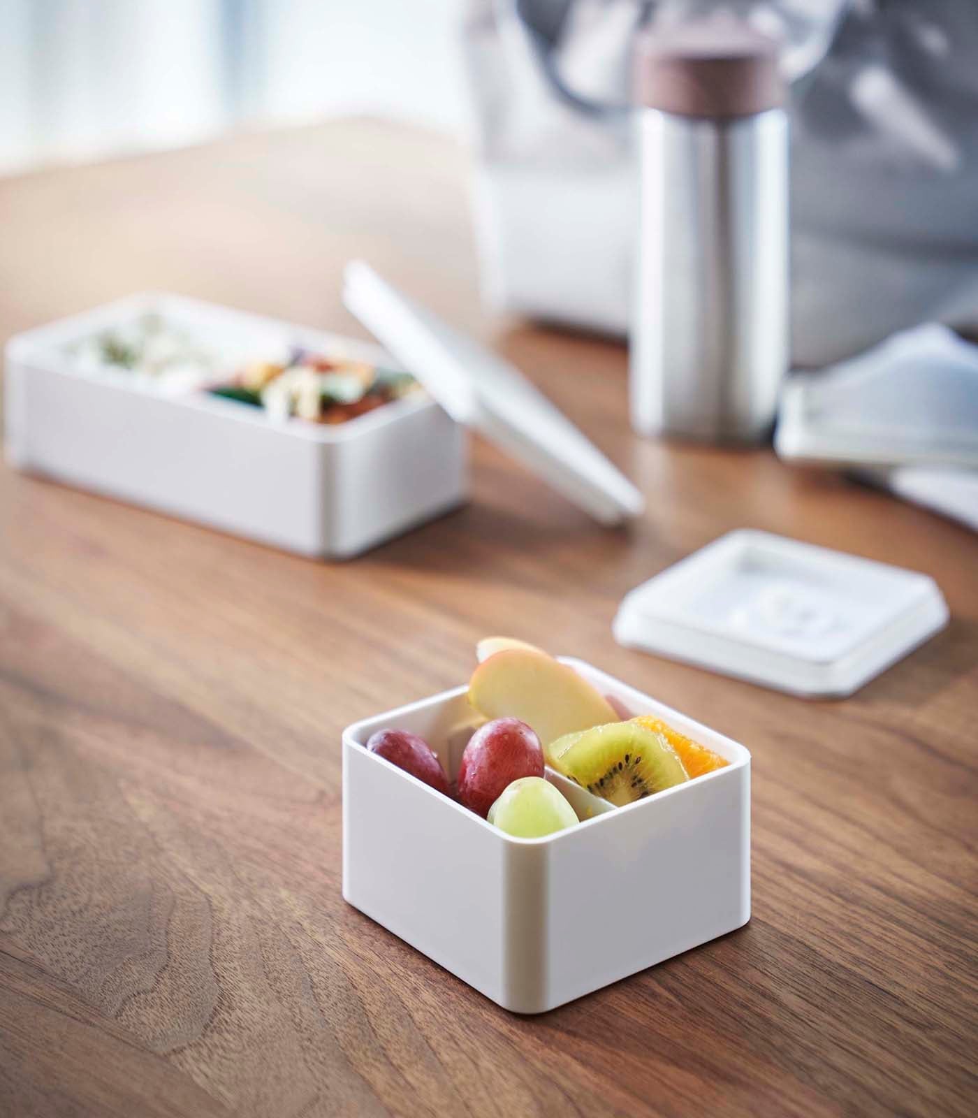 White bento box with fruits on a wooden table