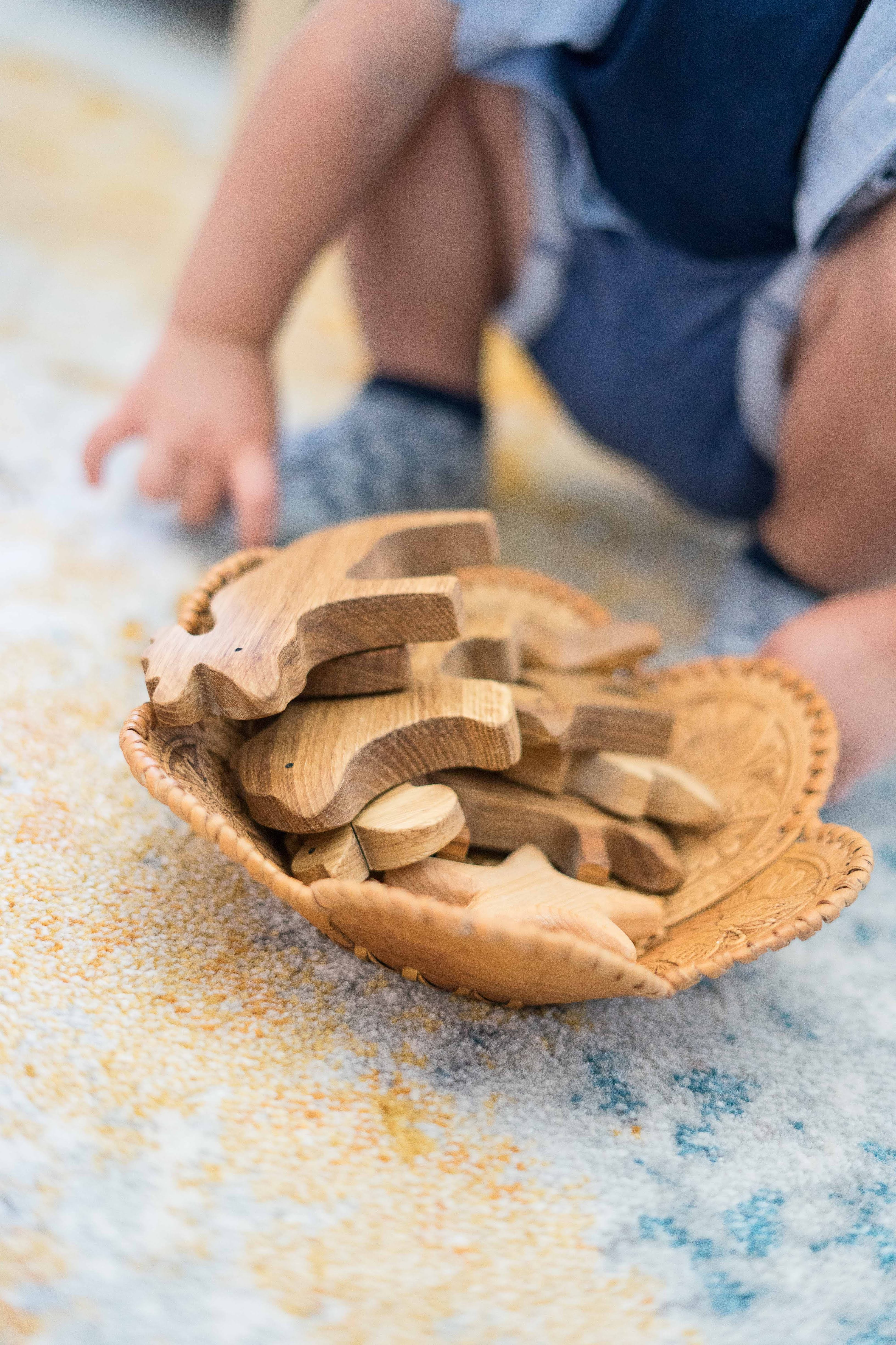 Wooden animal toys in a shell-shaped container on a sandy surface with a child in the background.