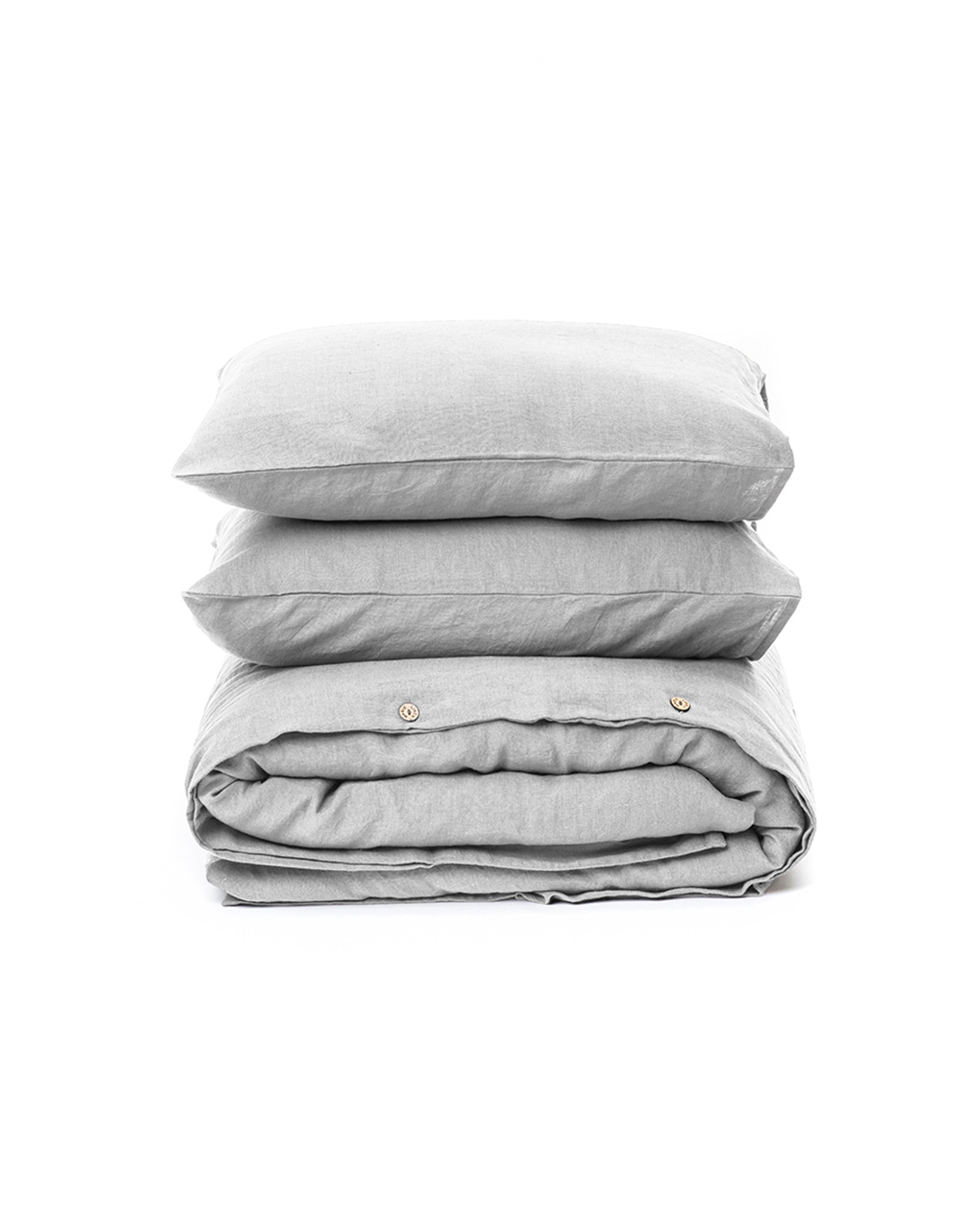 Stack of light gray bedding including a duvet and two pillows on a white background