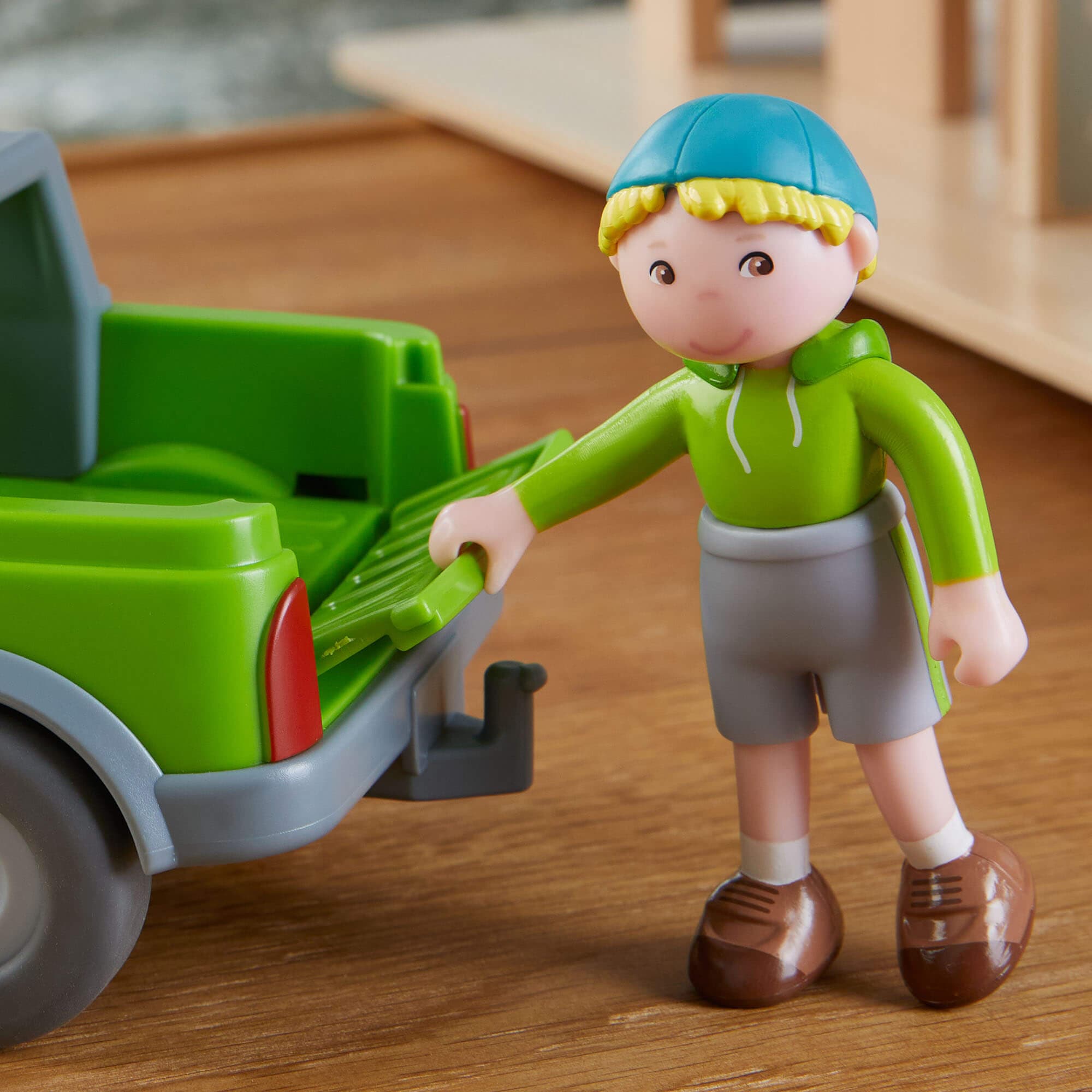 Toy figure of a child with a green toy truck on a wooden surface