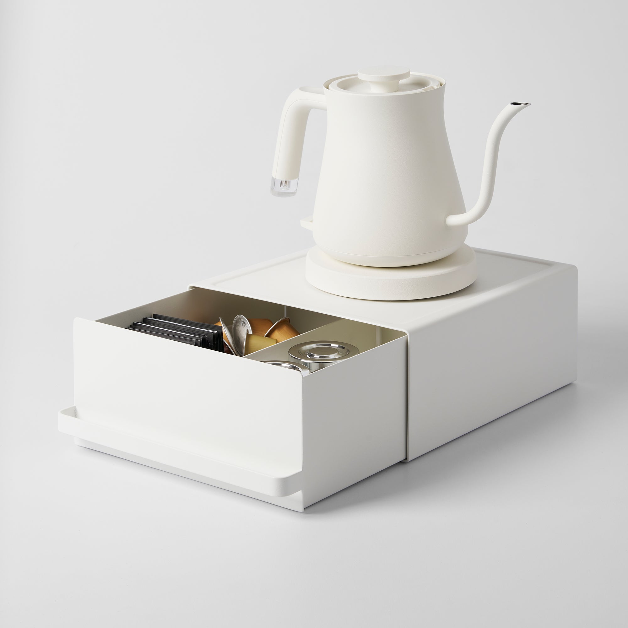 White electric kettle on a white stand with a small drawer containing tea bags and accessories.