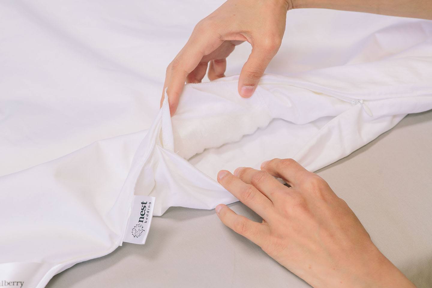Person folding a white garment with 'nest' label on a light surface