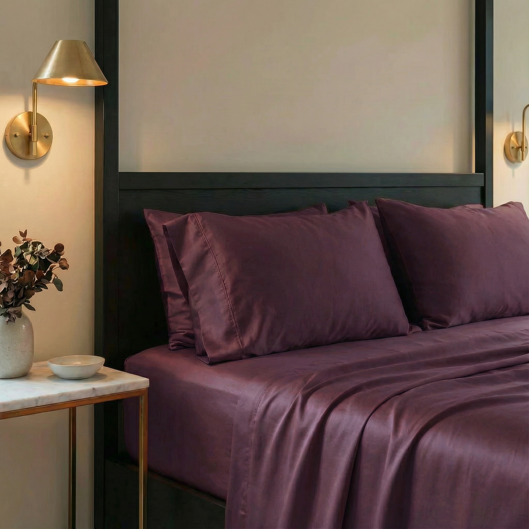 Bed with purple bedding in a bedroom setting with wall lights and decor.