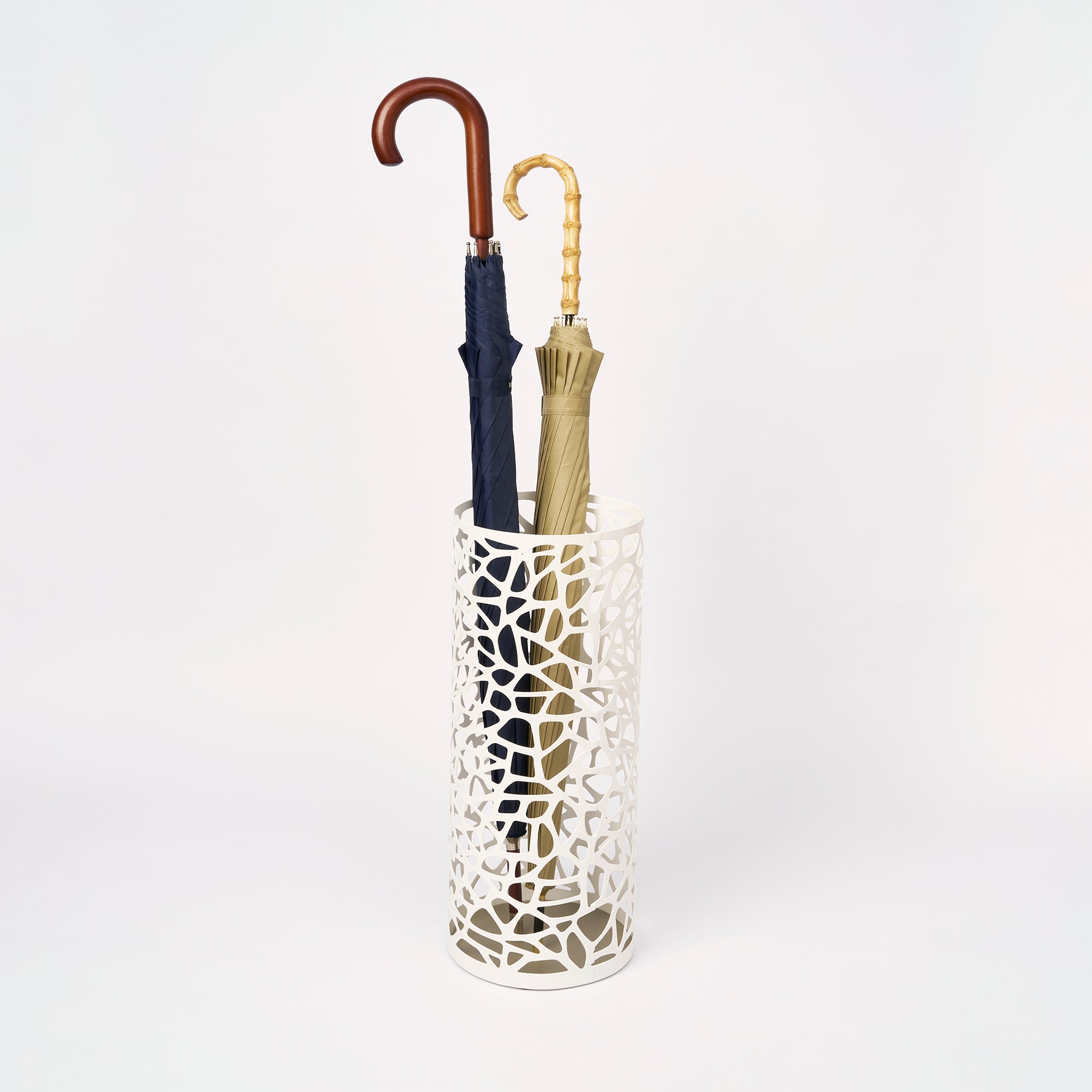 White umbrella stand holding two umbrellas on a light gray background