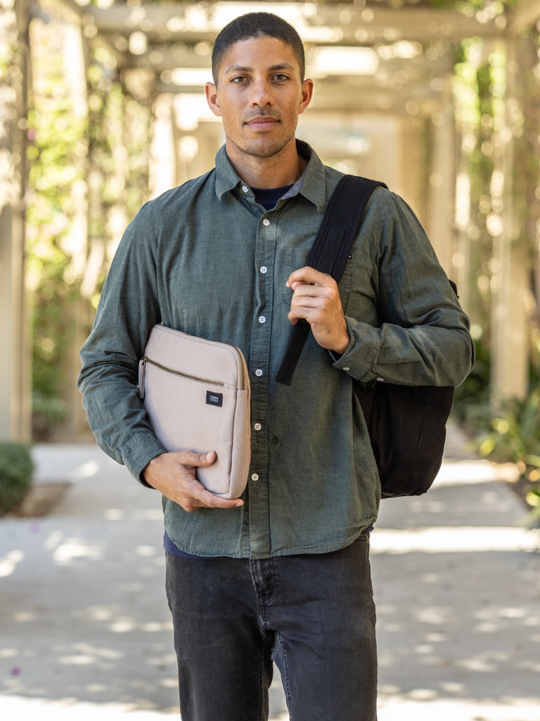 Man holding a beige laptop case and black backpack outdoors