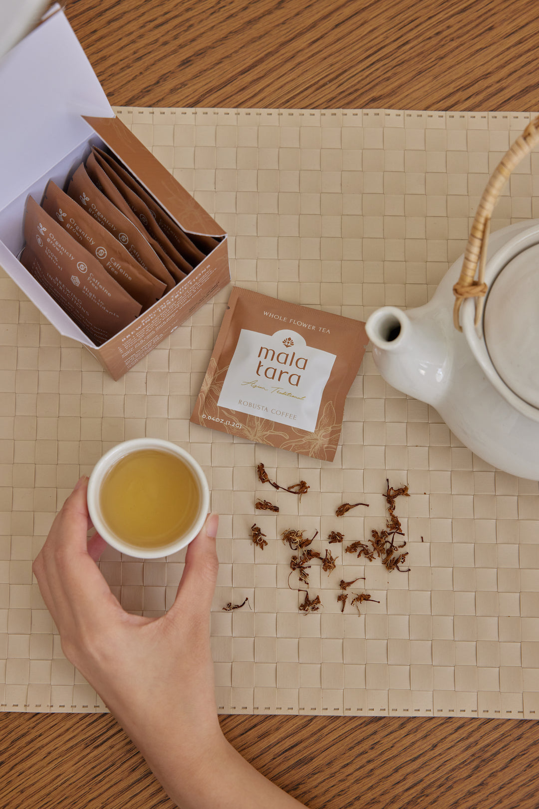 Tea cup with tea leaves, Mala Tara tea packaging, and teapot on a woven mat.