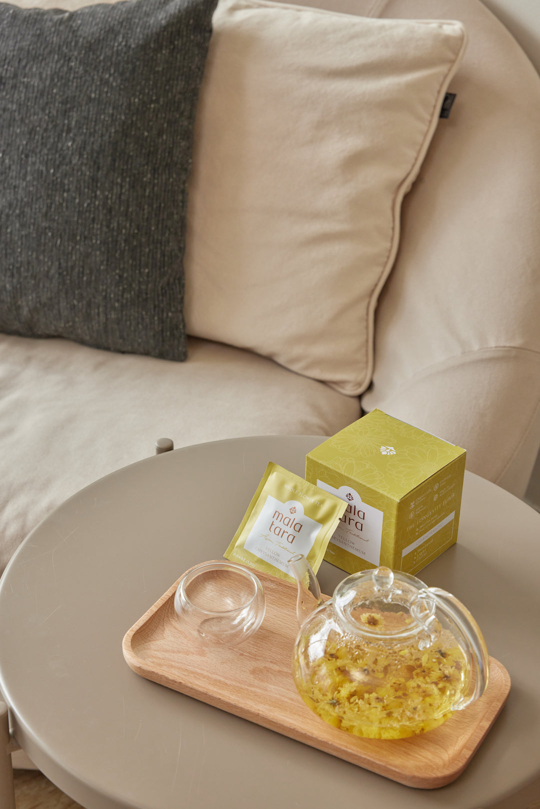 Tea set on a wooden tray with a box of tea bags on a beige sofa.