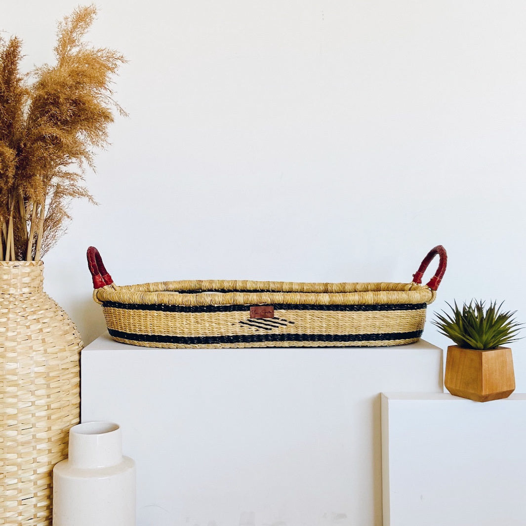Woven basket with red handles on a white surface with decorative items.
