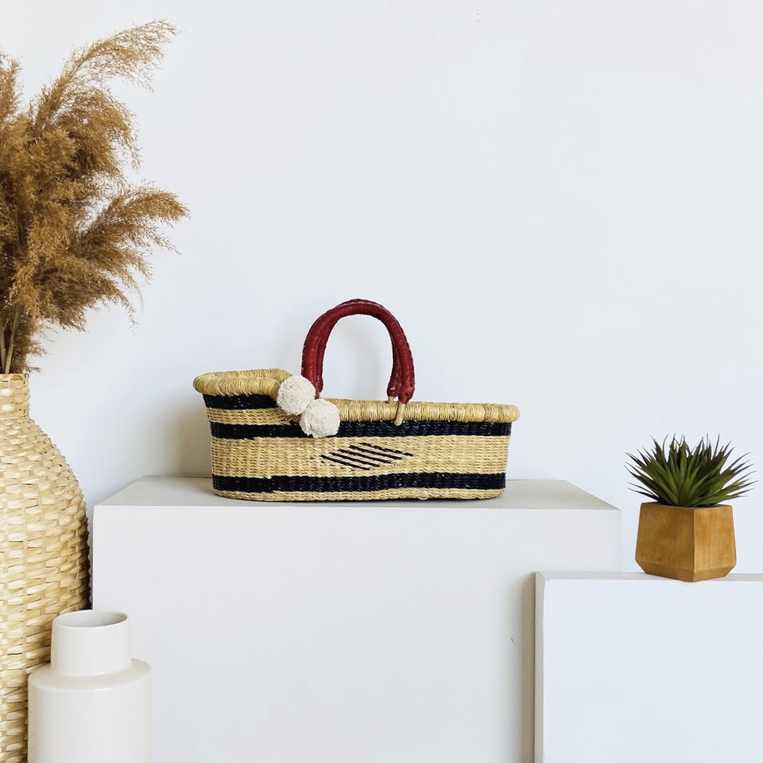 Woven basket with black and red accents on a white surface, surrounded by decorative items.