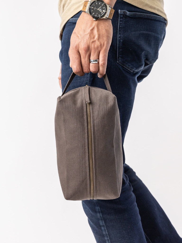 Person holding a brown leather toiletry bag with a white background