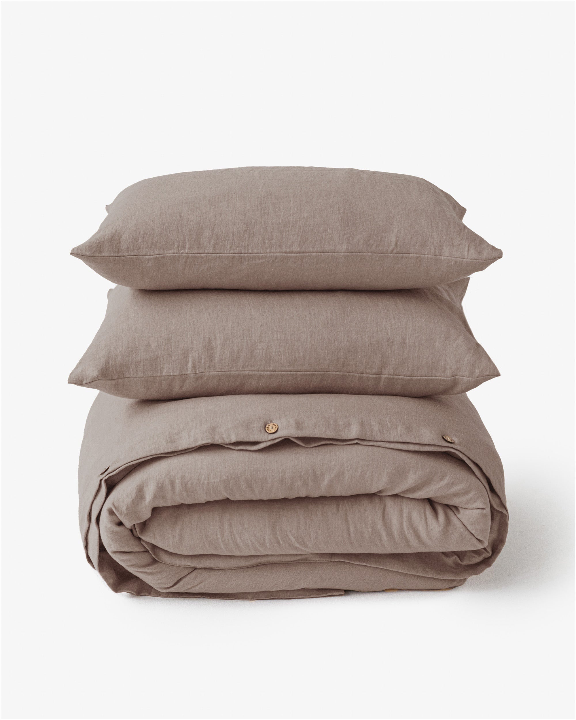 Stack of beige bedding with a duvet and two pillows on a white background