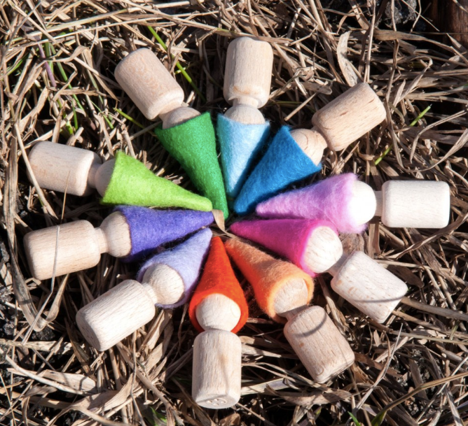 Colorful wooden cones with chisel tips arranged in a circle on dry grass.