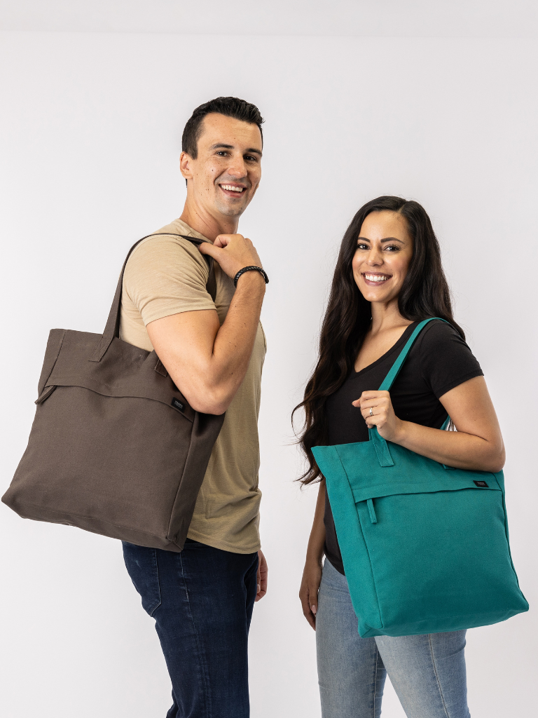 Man and woman holding brown and teal tote bags against a white background