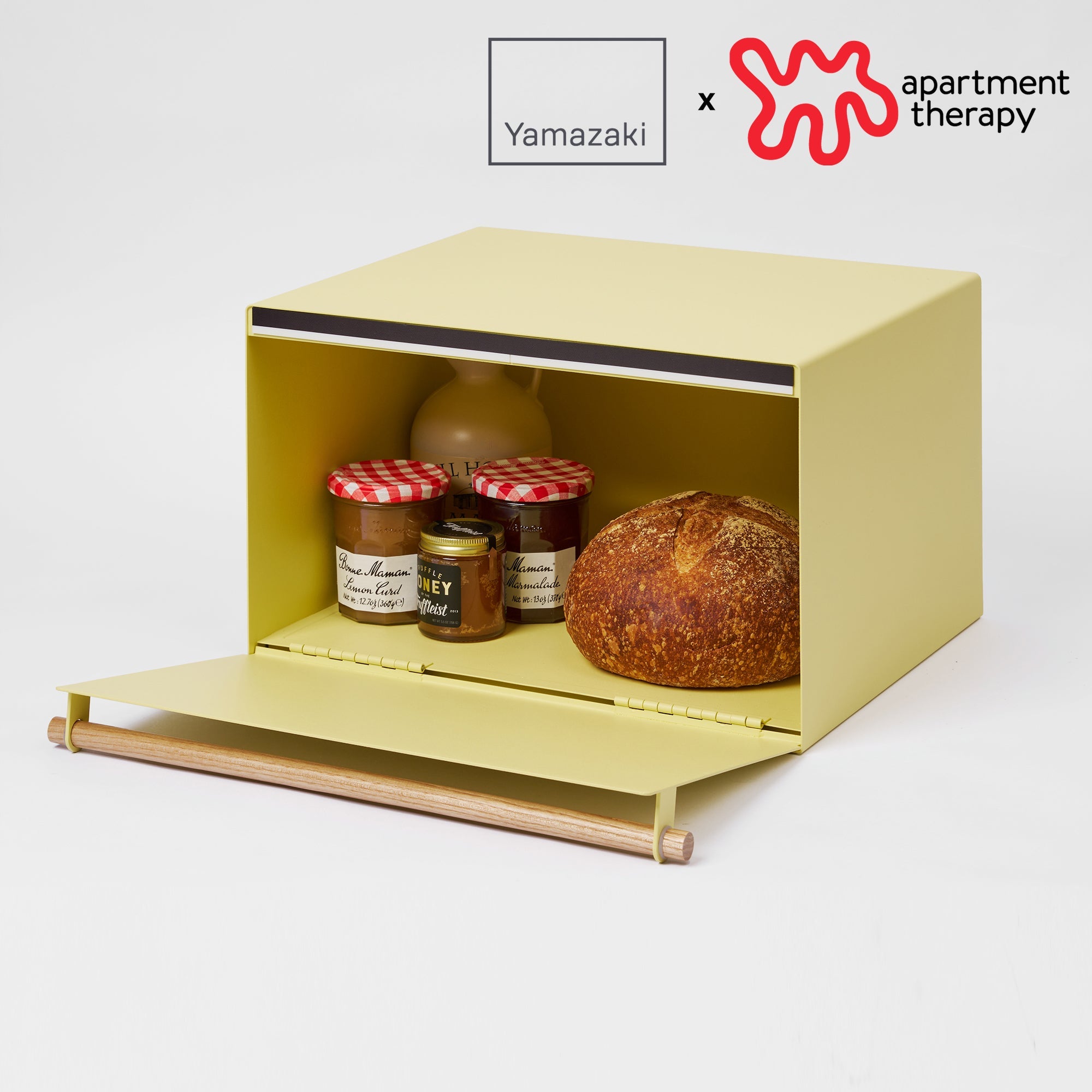 Yellow bread box with a loaf of bread and jars on a white background, featuring Yamazaki and Apartment Therapy logos.
