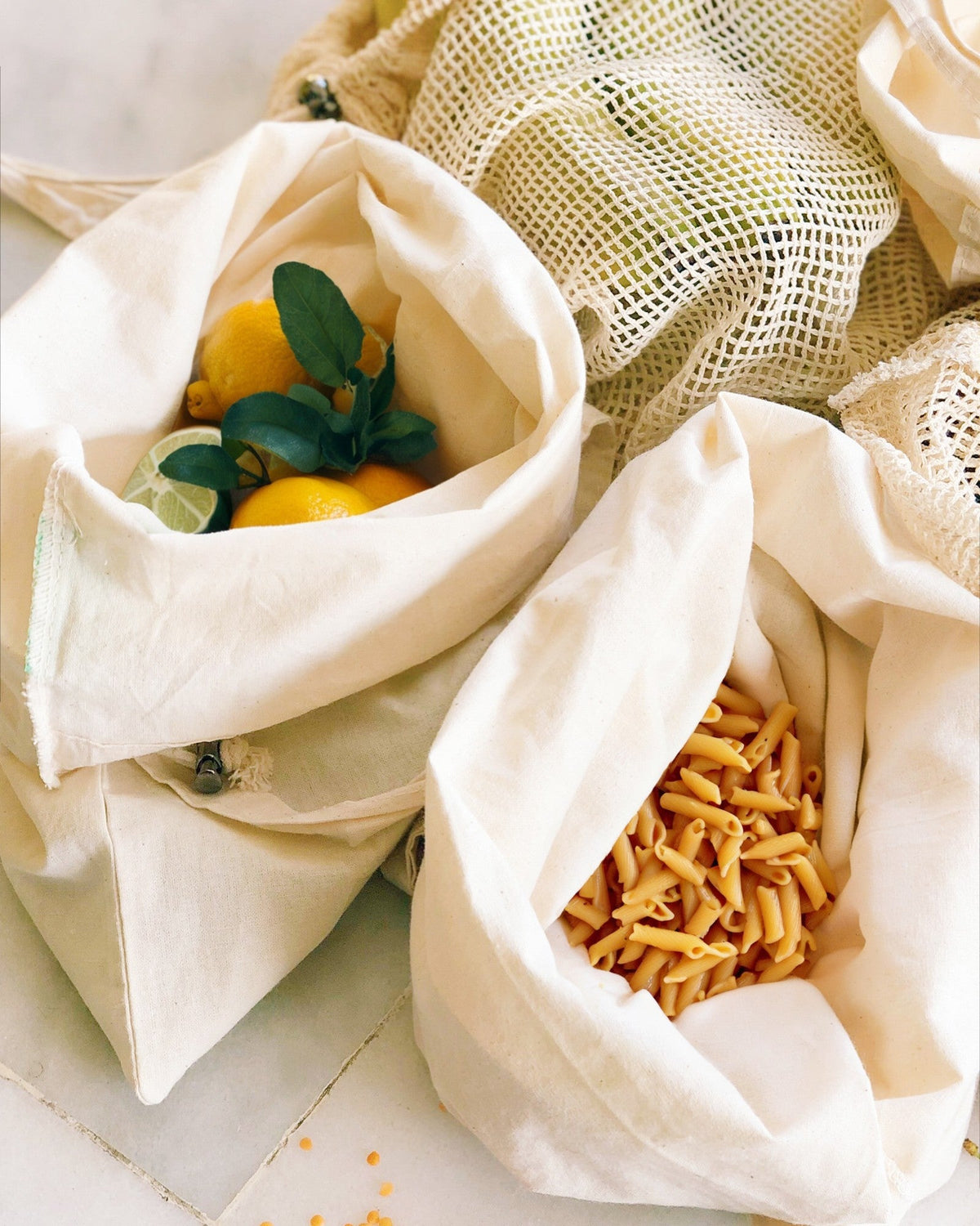 Fabric bags with lemons and pasta on a light surface