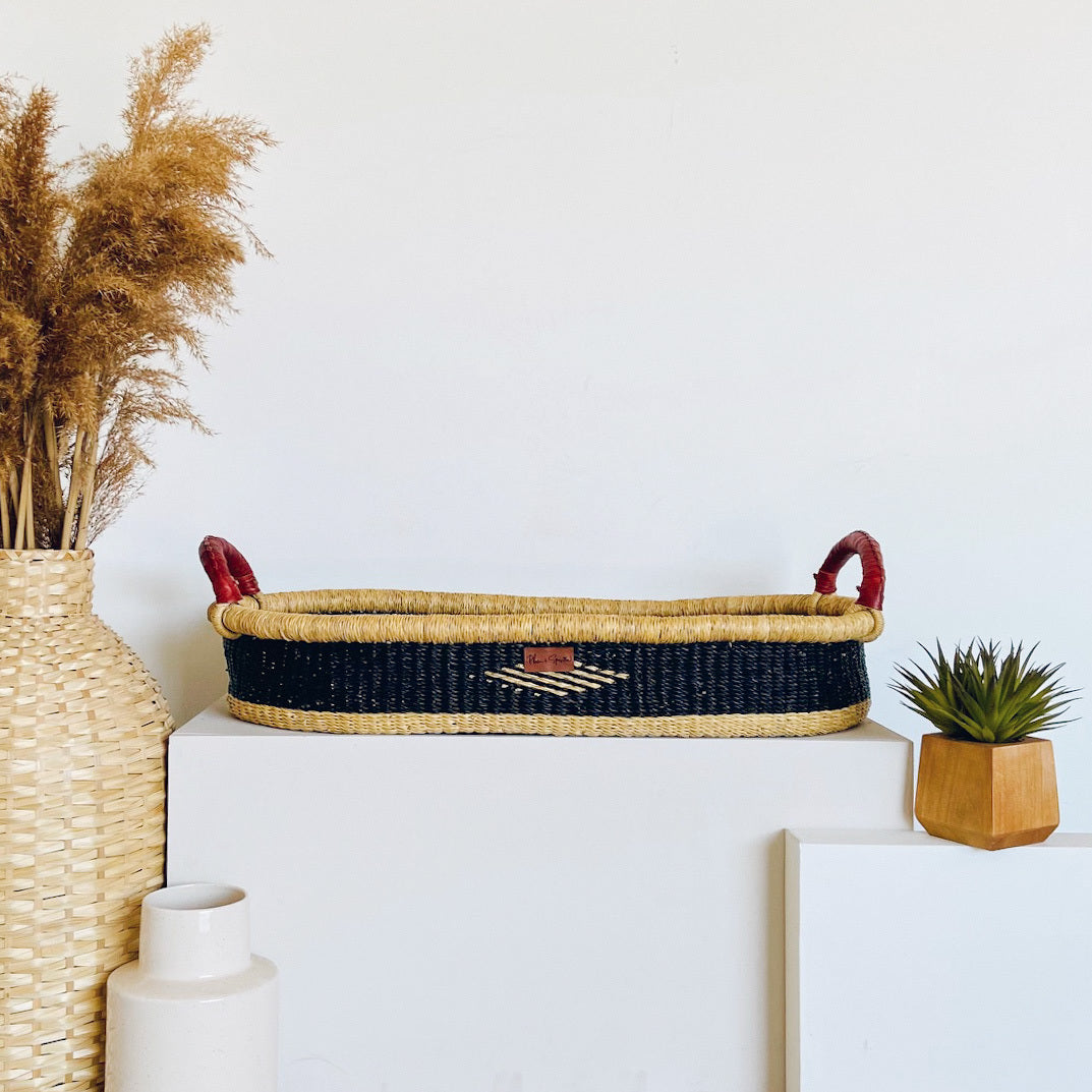 Woven basket with handles on a white surface, surrounded by decorative items.