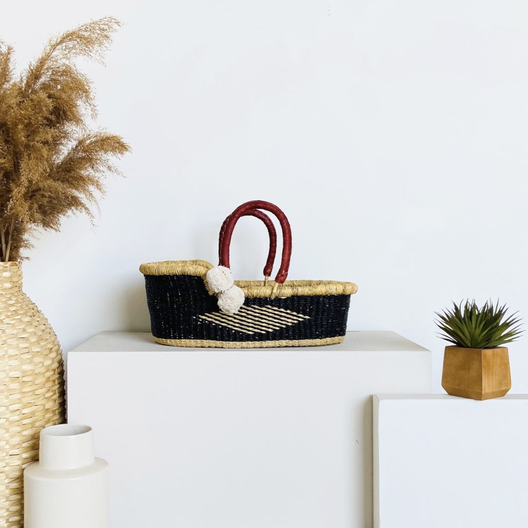 Woven basket with black interior and red handles on a white surface with decorative items.