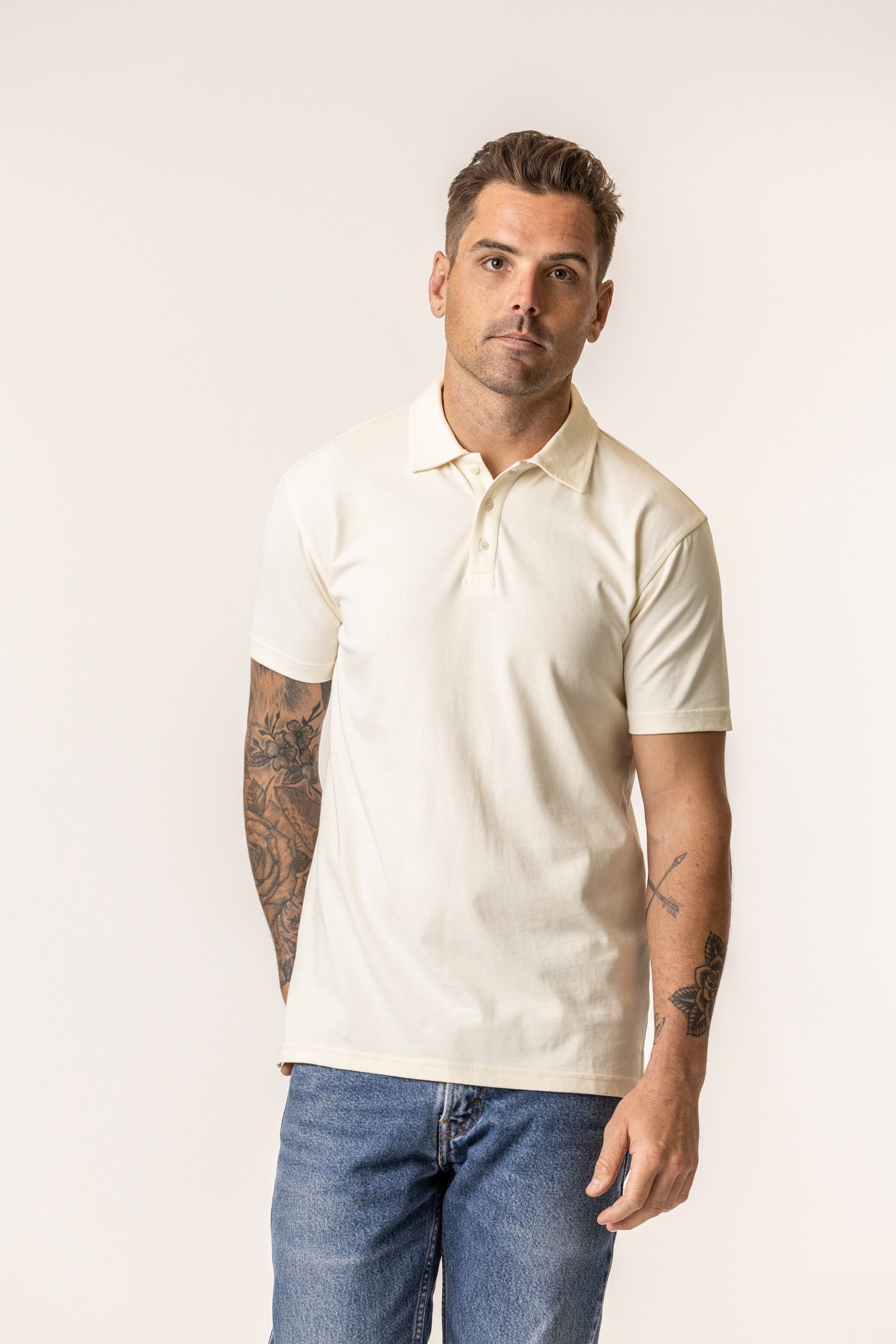 Man wearing a beige polo shirt and blue jeans against a white background
