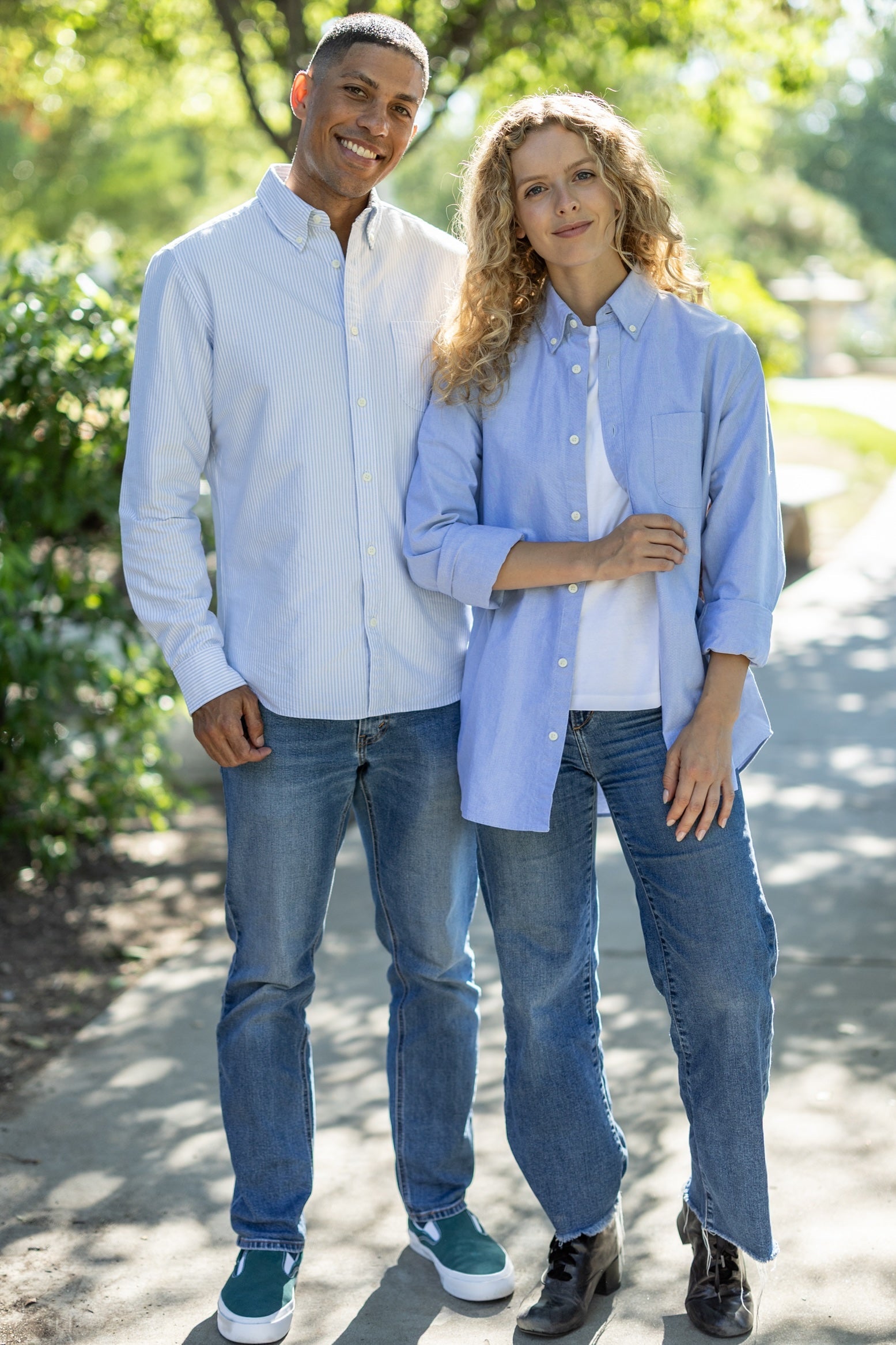 Two people wearing matching light blue shirts and jeans standing outdoors.
