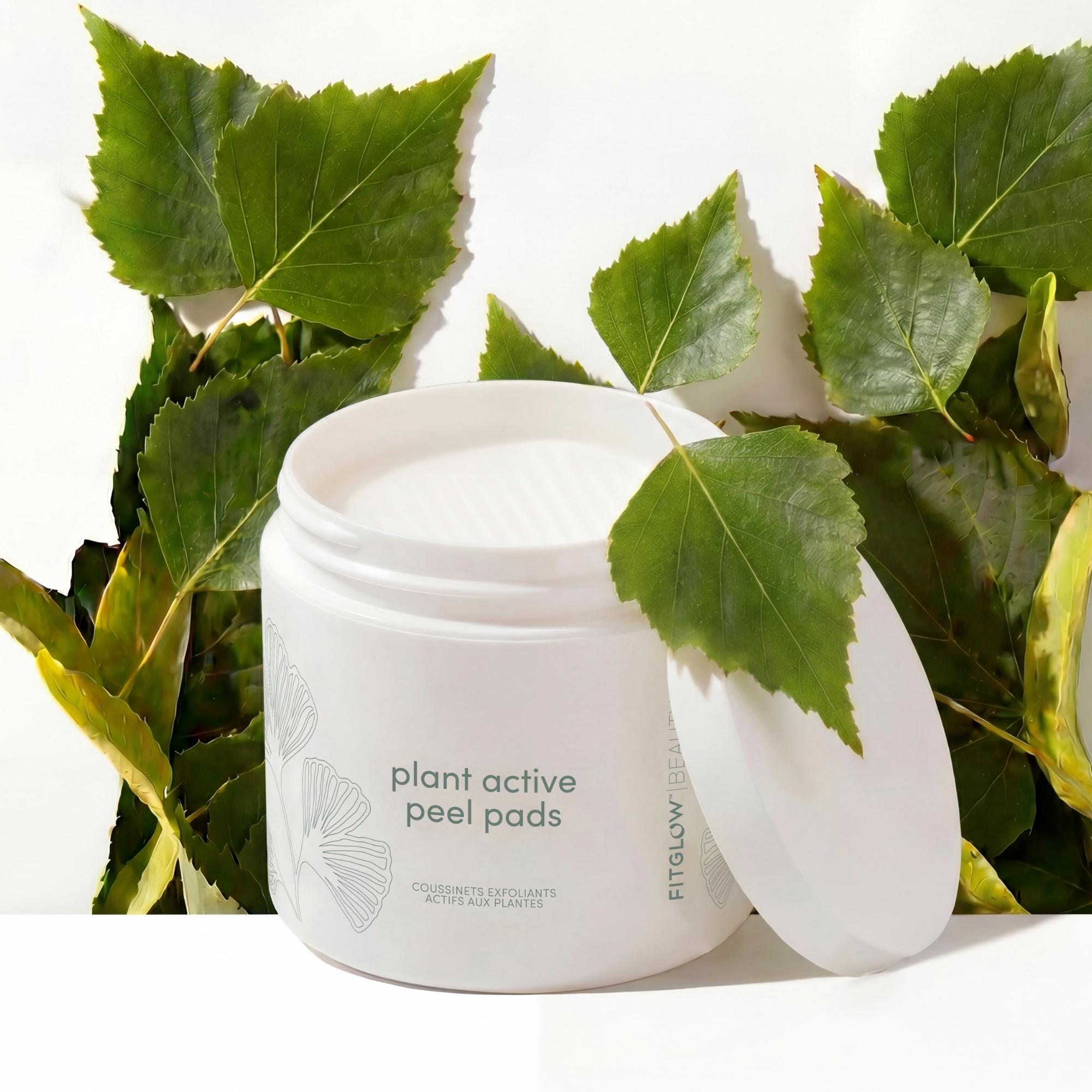 Jar of 'plant active peel pads' surrounded by green leaves on a white background