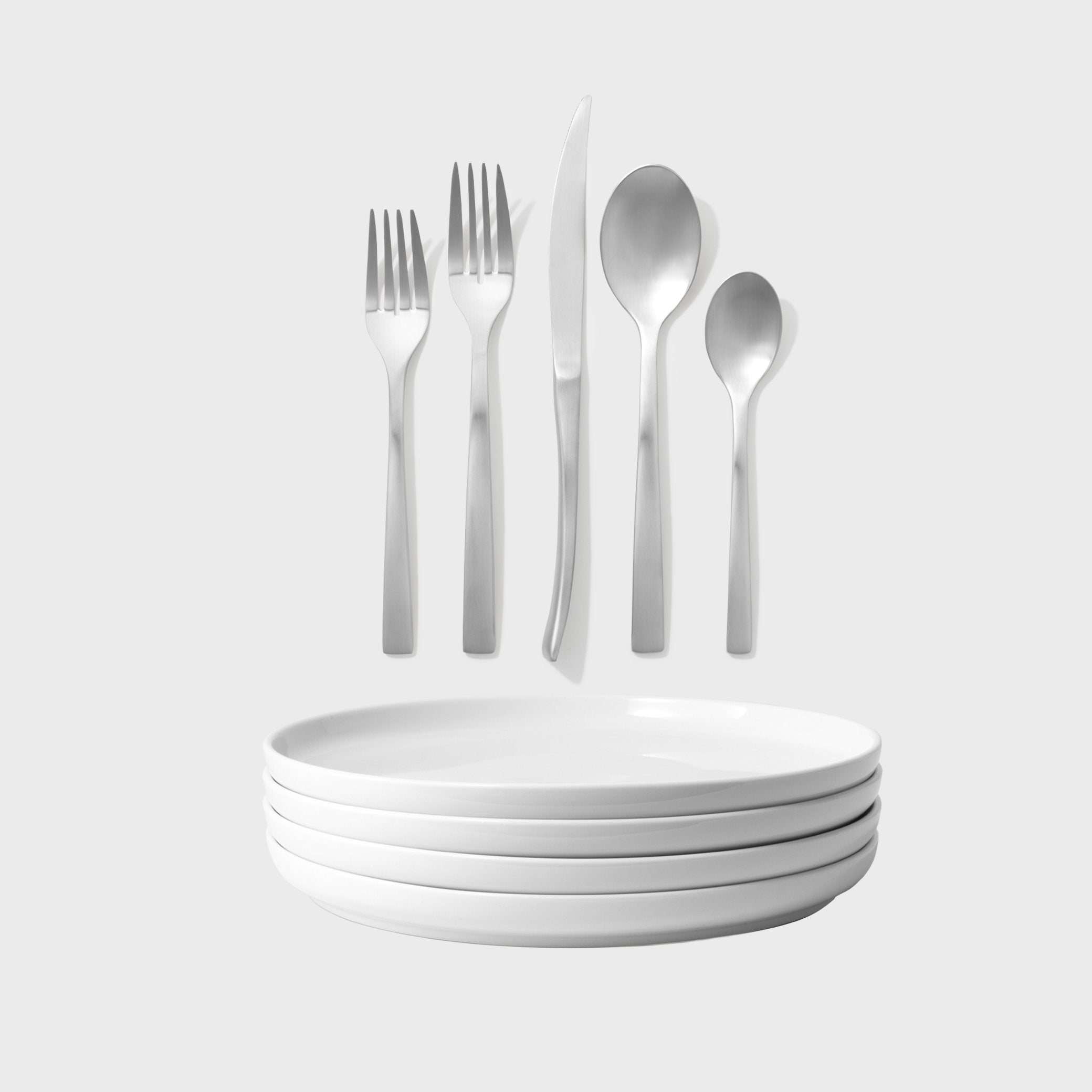 Set of silver cutlery and white plates on a light gray background