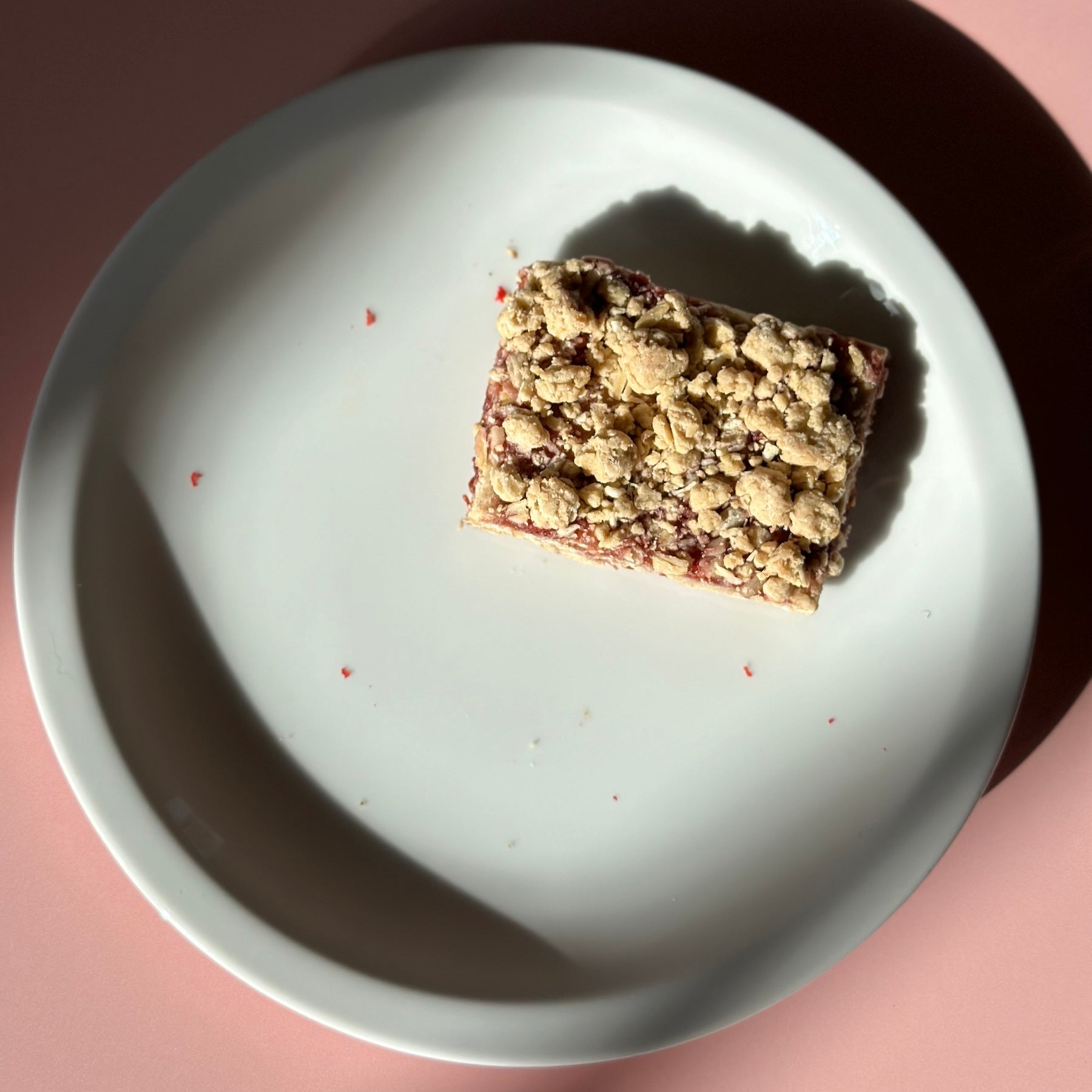 Square dessert bar with crumbly topping on a white plate against a pink background