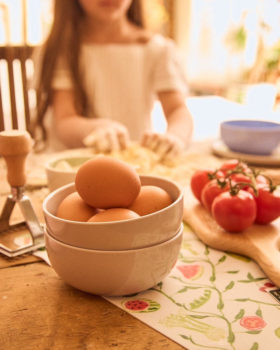 Bowl of eggs on a table with tomatoes and a person in the background