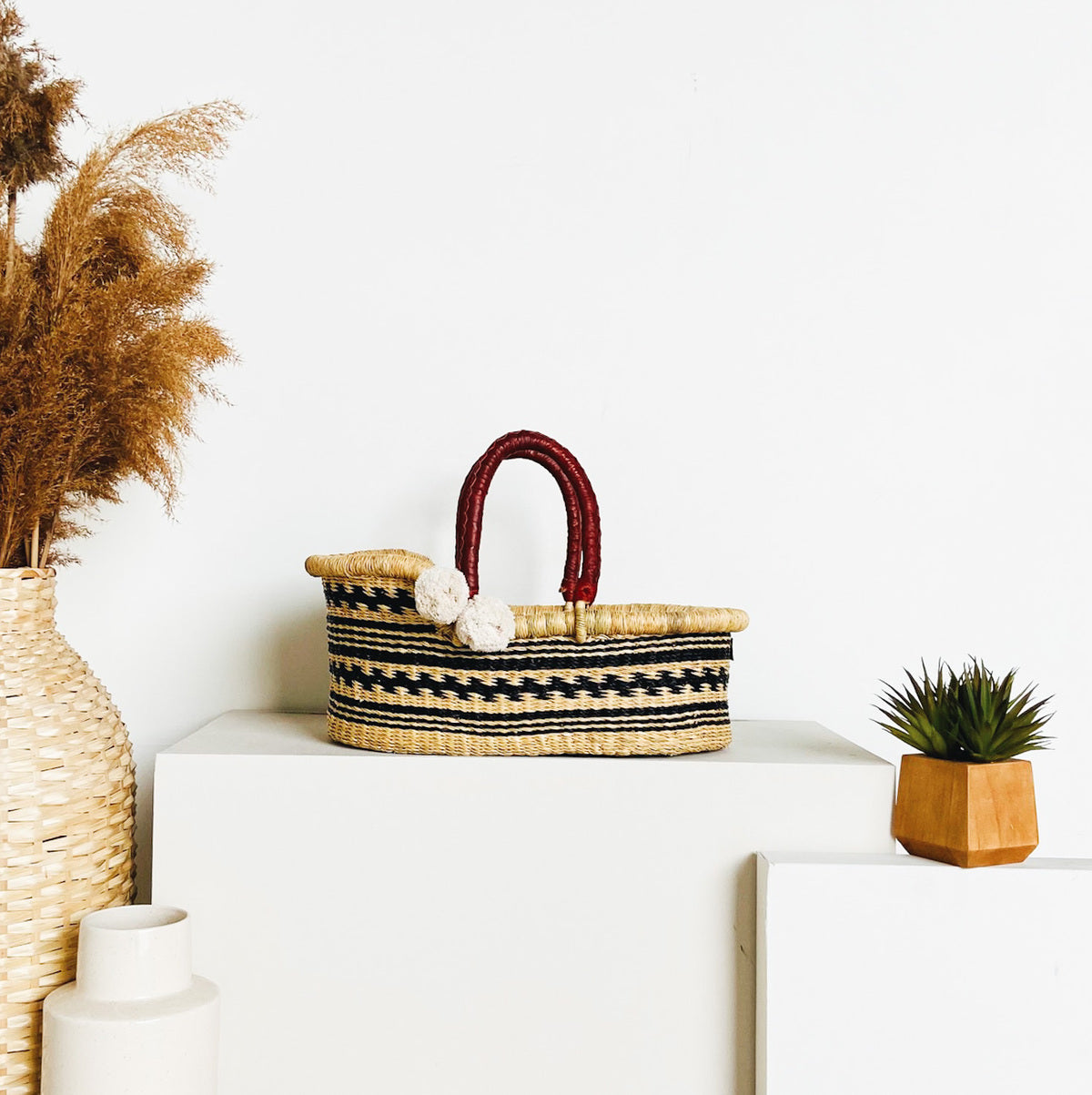 Woven basket with a red handle on a white surface, surrounded by decorative items.