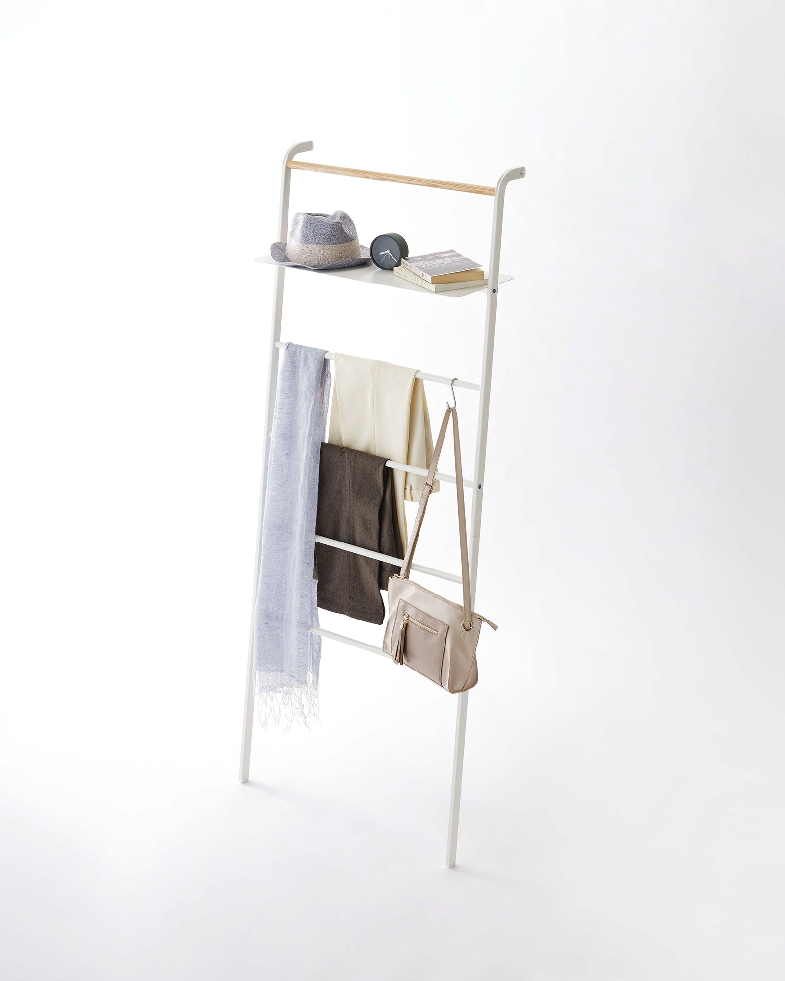 White clothing rack with shelves holding a bag, books, and a hat on a white background