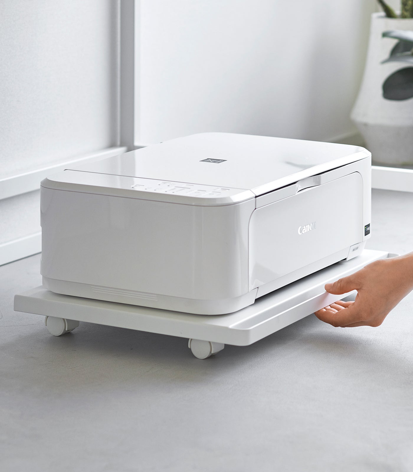 White printer on a stand with a hand holding the edge, in a minimalistic room.