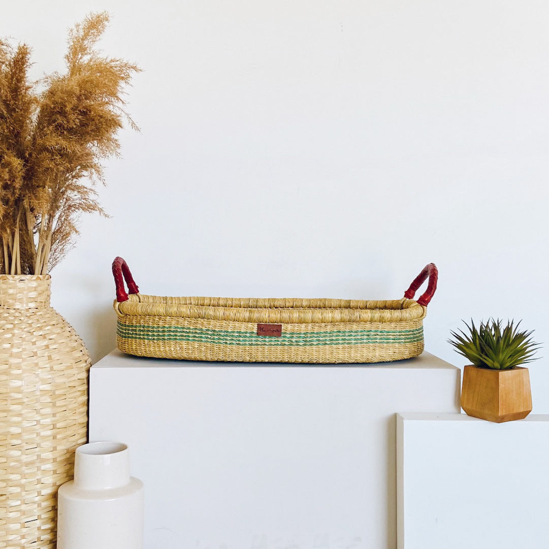 Woven basket with handles on a white surface, surrounded by decorative items.