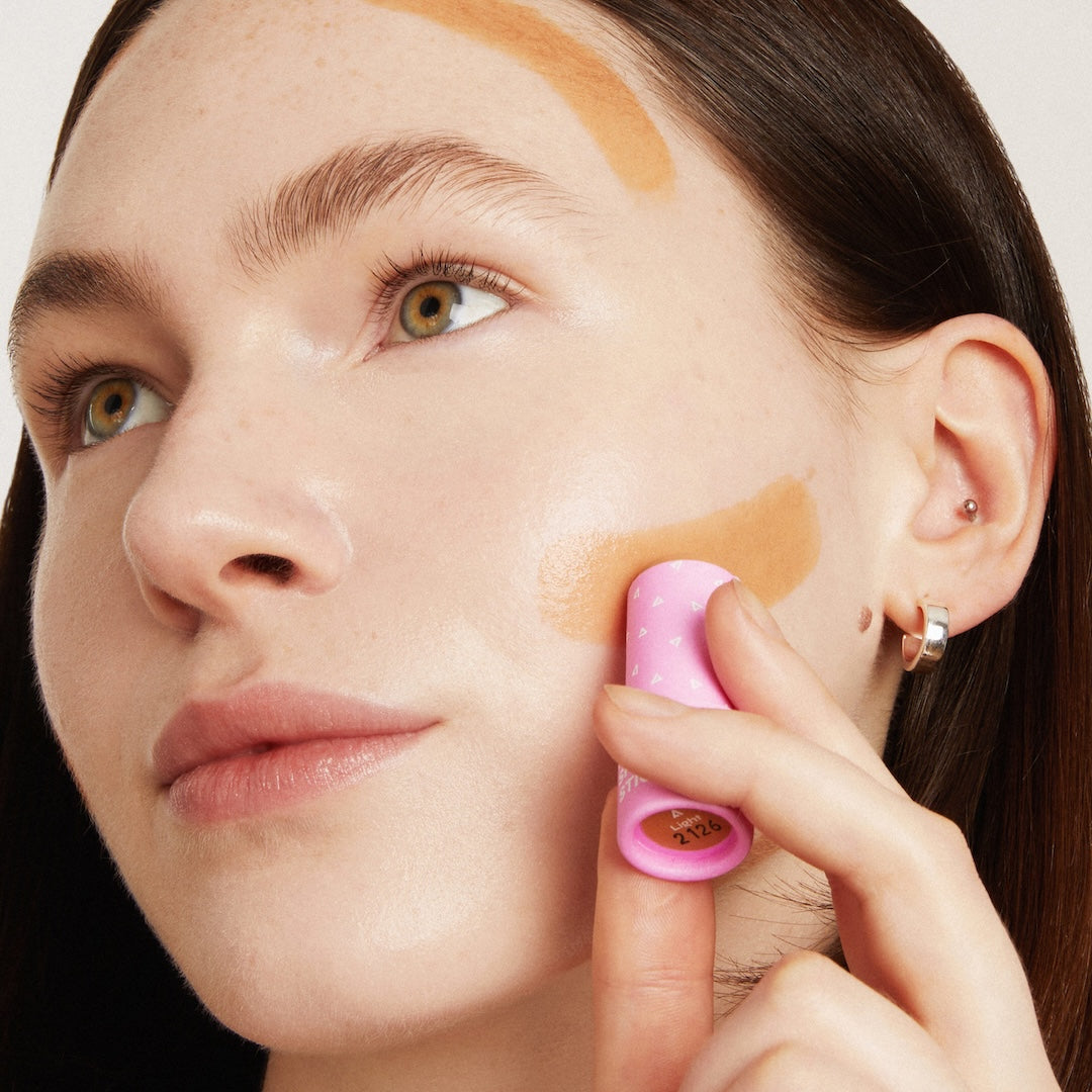 Woman applying makeup with a pink sponge applicator on a neutral background