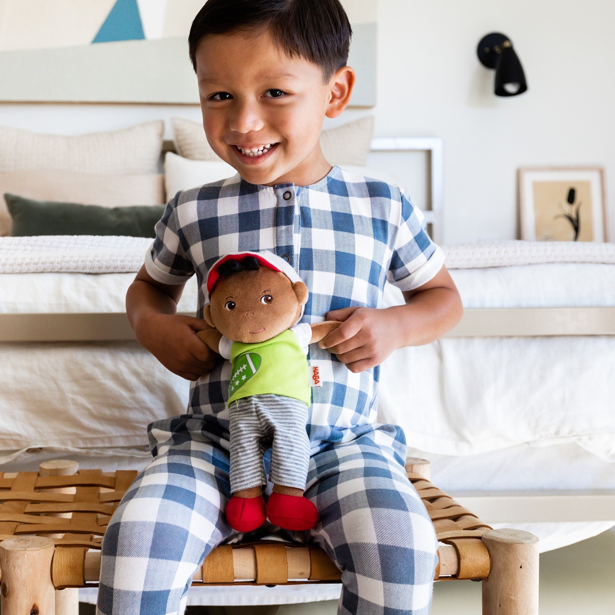 Child in checkered pajamas holding a plush toy on a wooden stool.