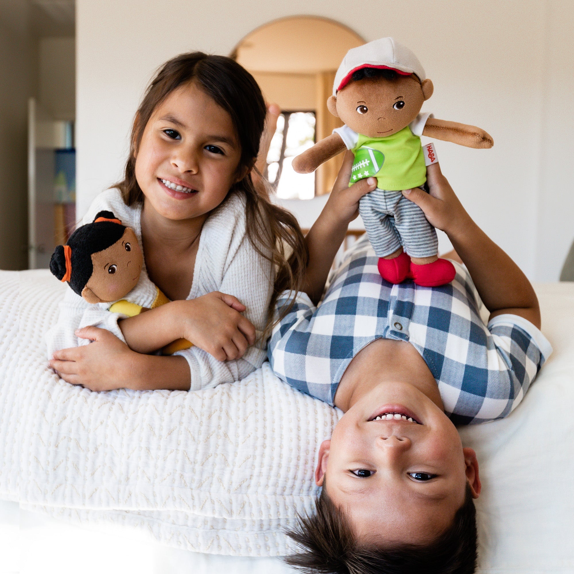 Two children playing with dolls on a bed in a cozy room.