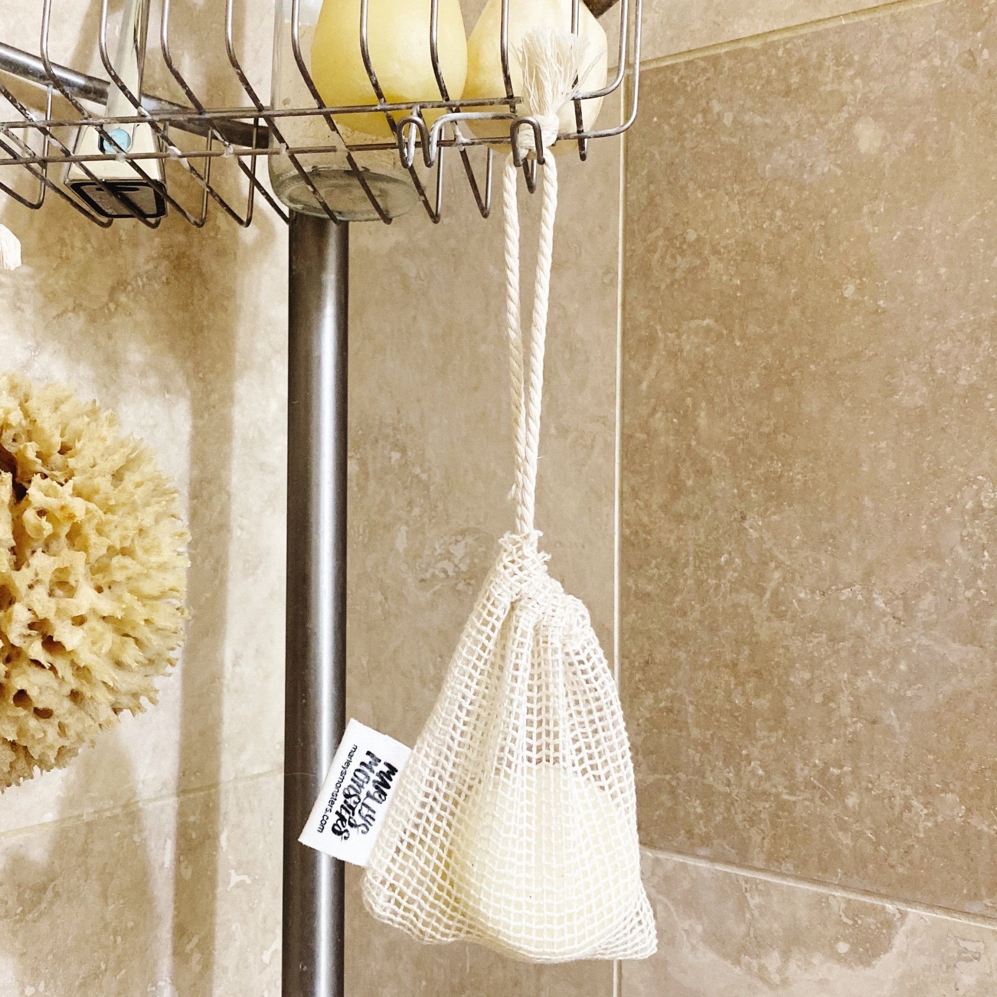 White mesh soap bag hanging from a shower caddy with a beige tiled wall background