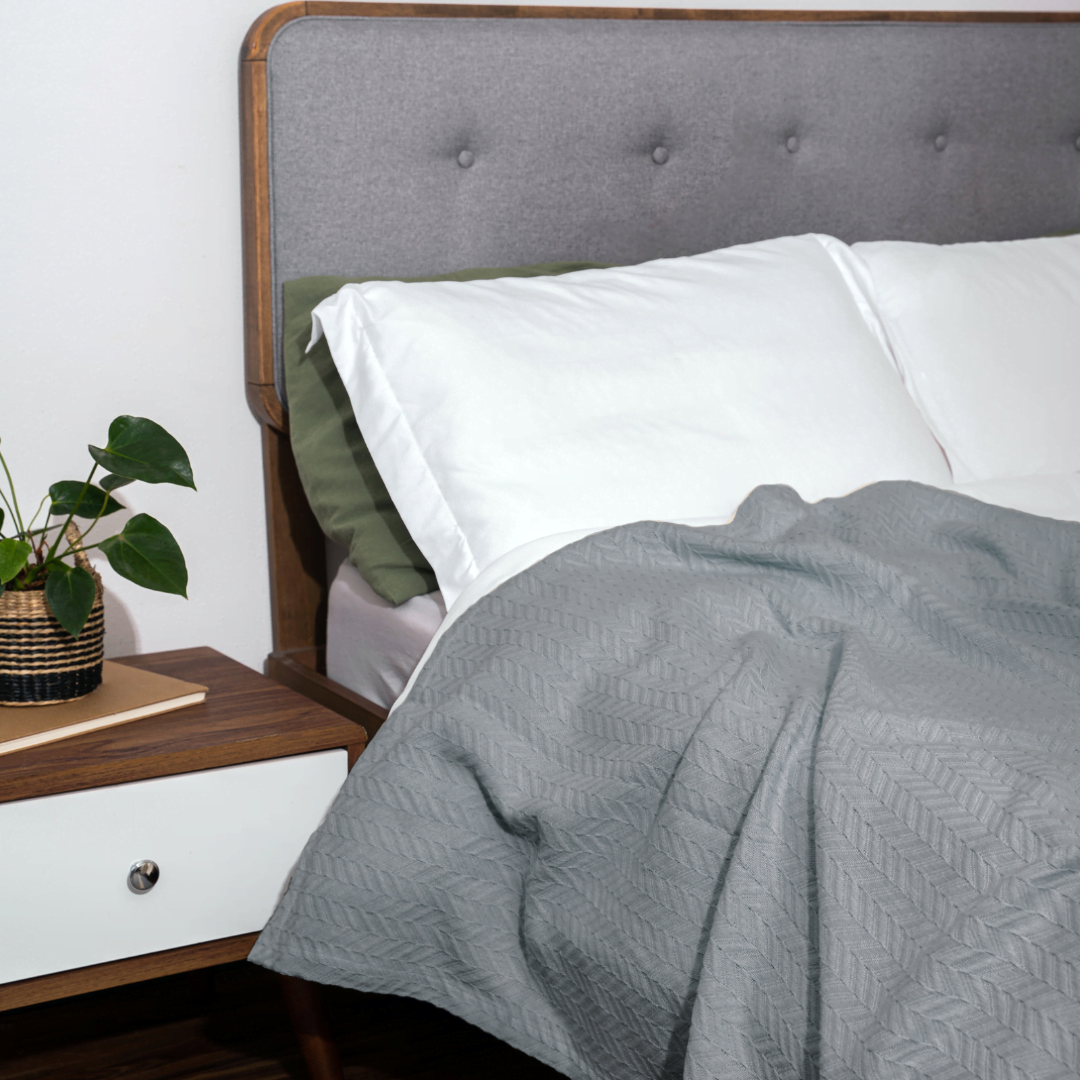 Gray textured blanket on a bed with a wooden headboard and nightstand.