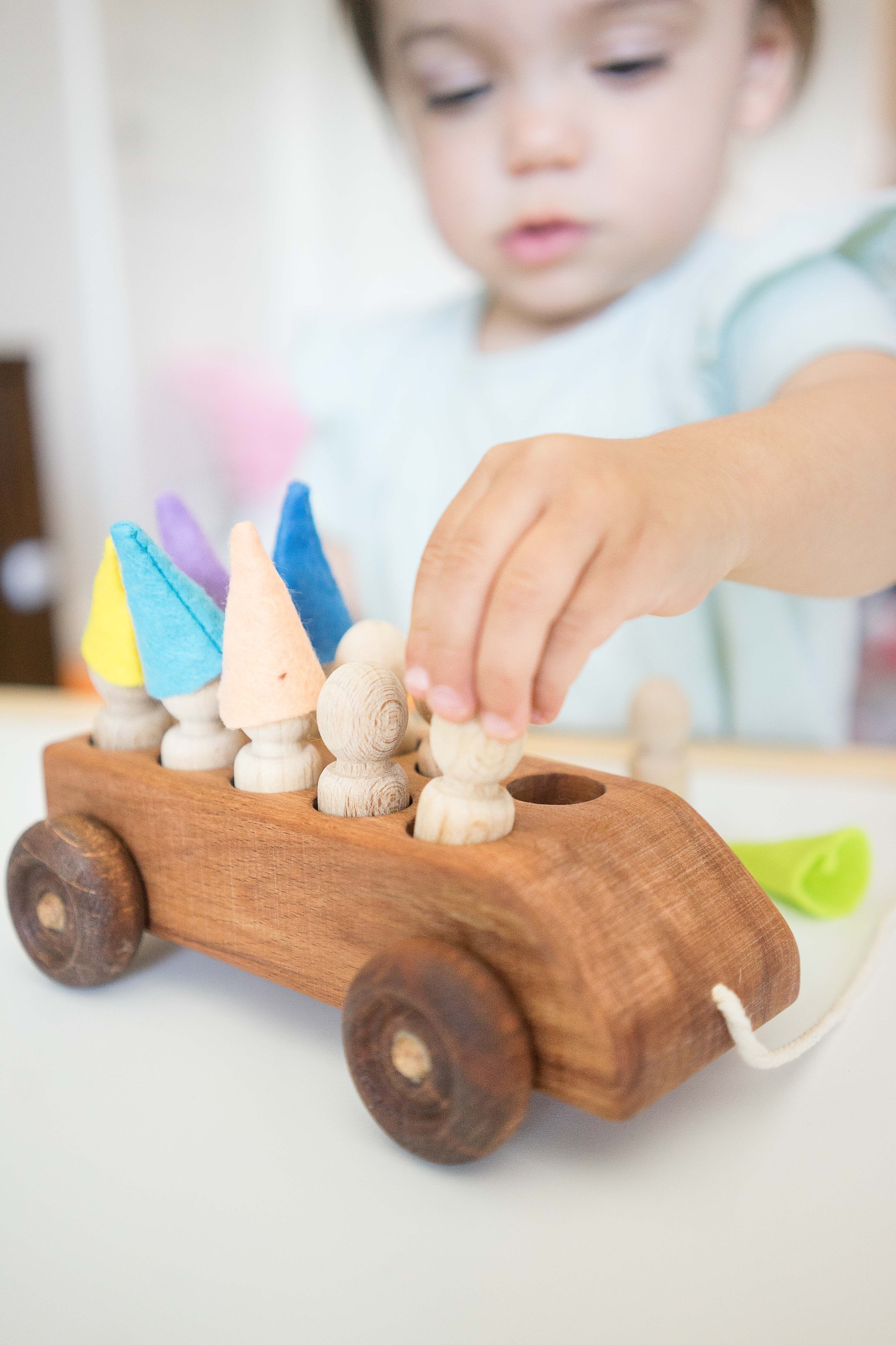 Child playing with a wooden toy car with colorful knobs.