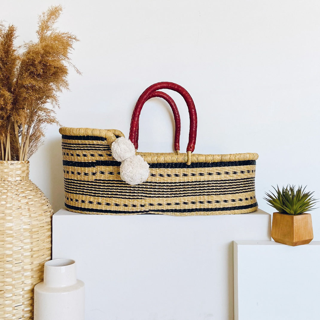Woven basket with red handles on a white surface, surrounded by decorative items.