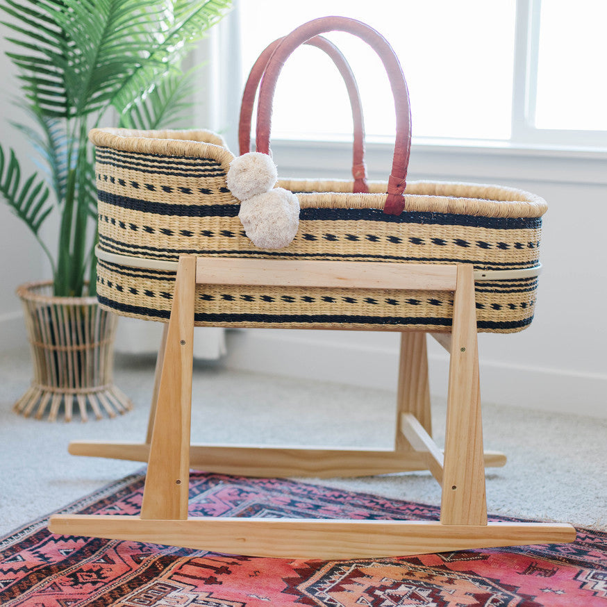 Wicker Moses basket with wooden stand on a patterned rug, plant in the background