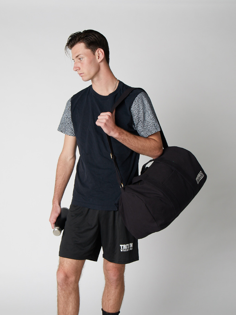 Man holding a black duffel bag against a plain background