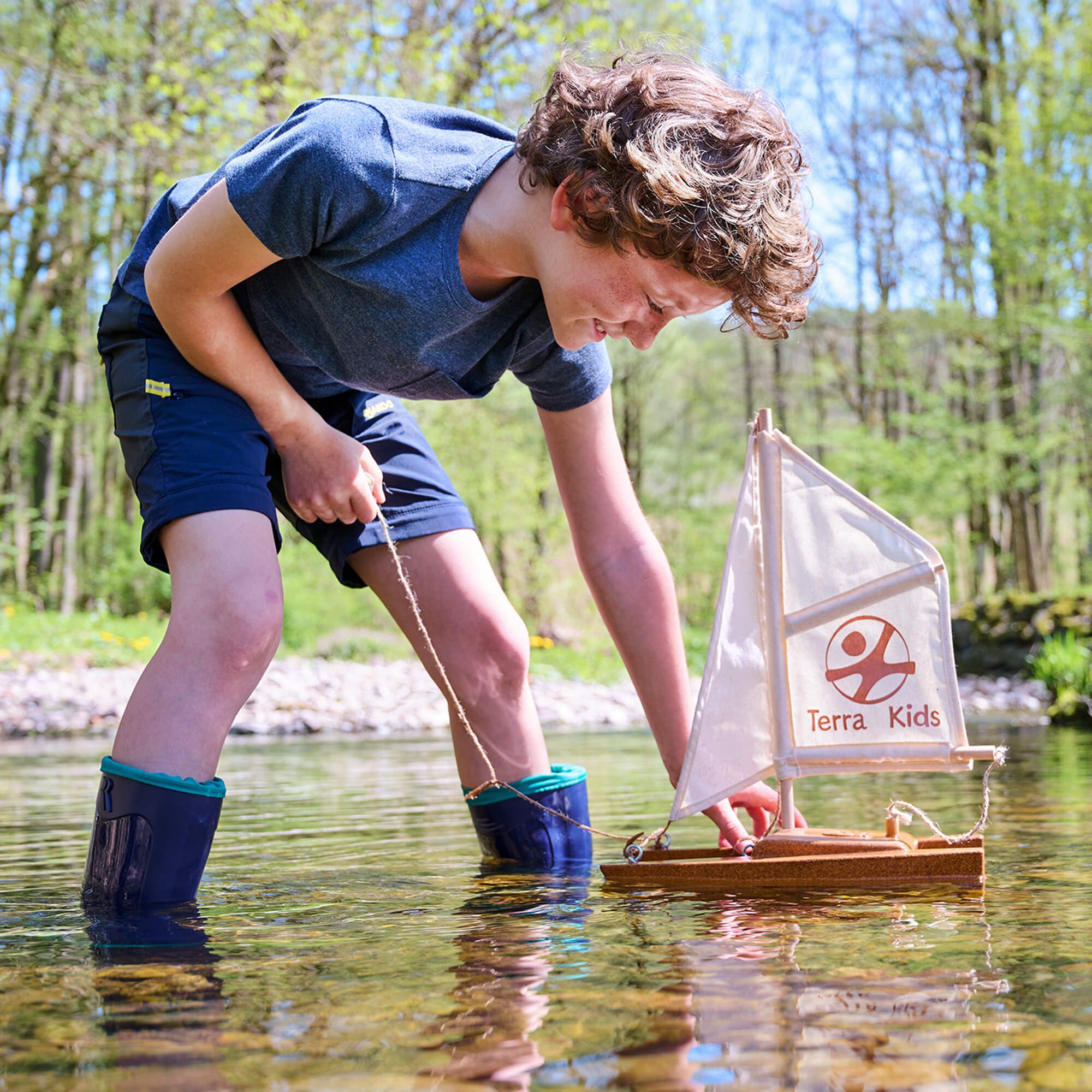 Child playing with a model sailboat in a natural setting