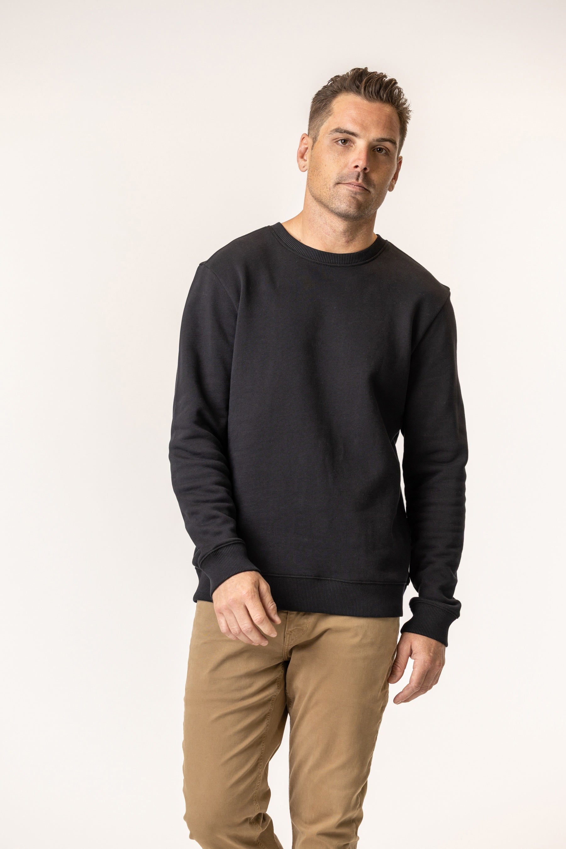 Man wearing a black sweater and beige pants on a white background