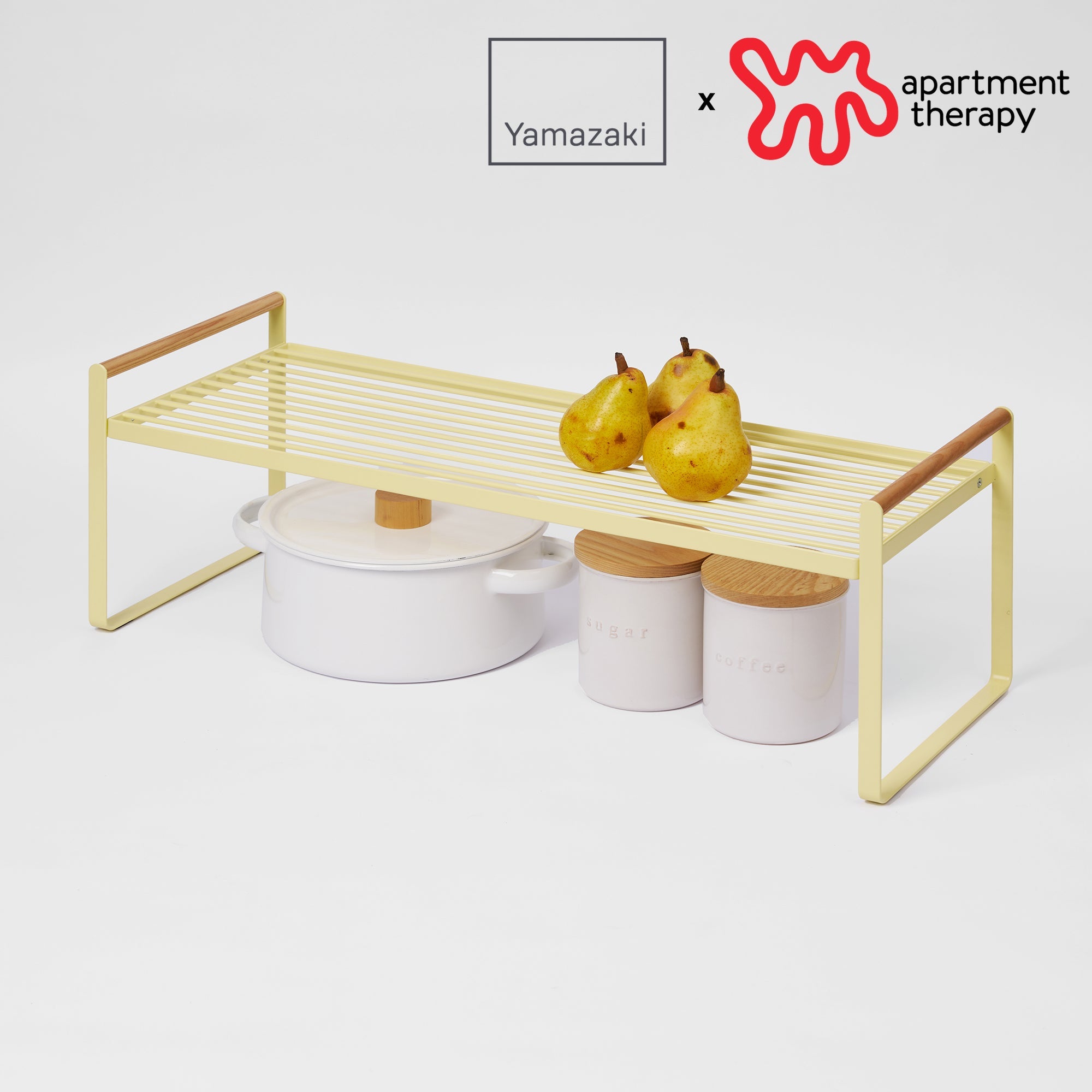 Small wooden shelf with white containers and pears on a light gray background, featuring Yamazaki and Apartment Therapy logos.