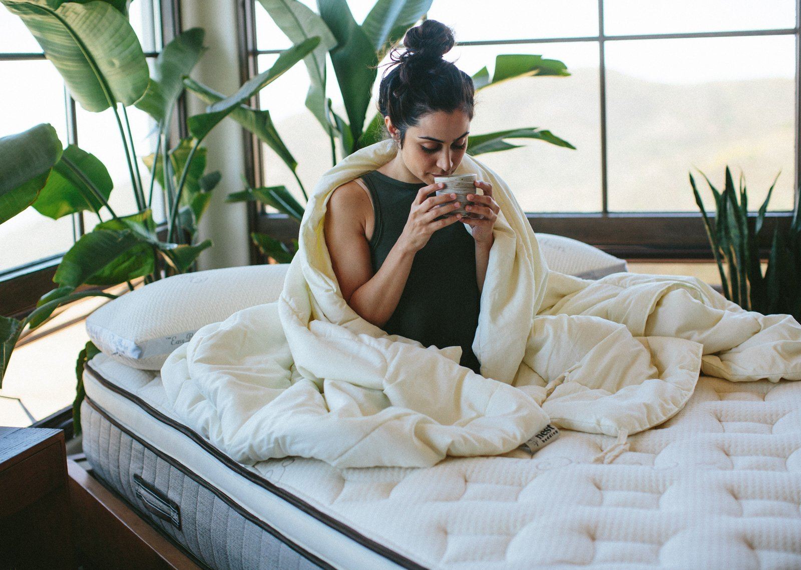 Woman wrapped in a blanket on a mattress with plants in the background