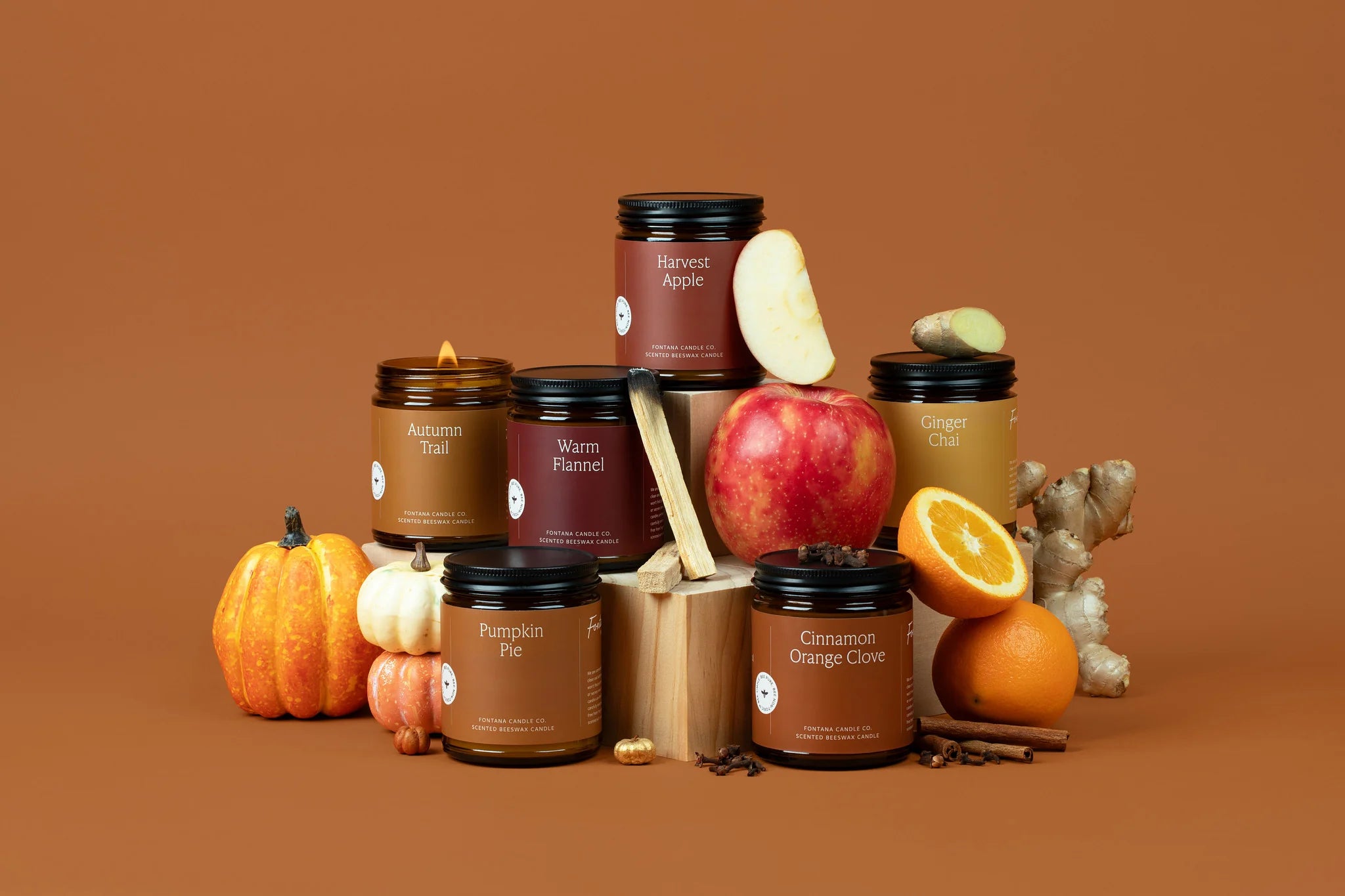 Collection of candles with autumn-themed packaging and ingredients on a brown background