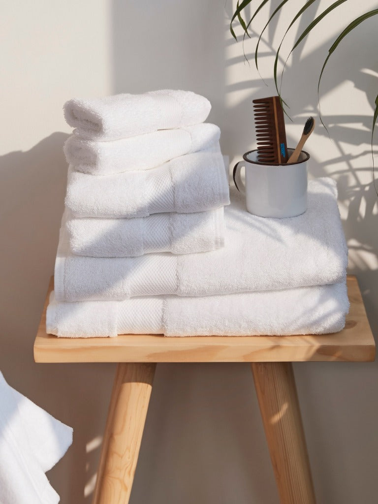 Stack of white towels on a wooden stool with a mug and comb in the background.