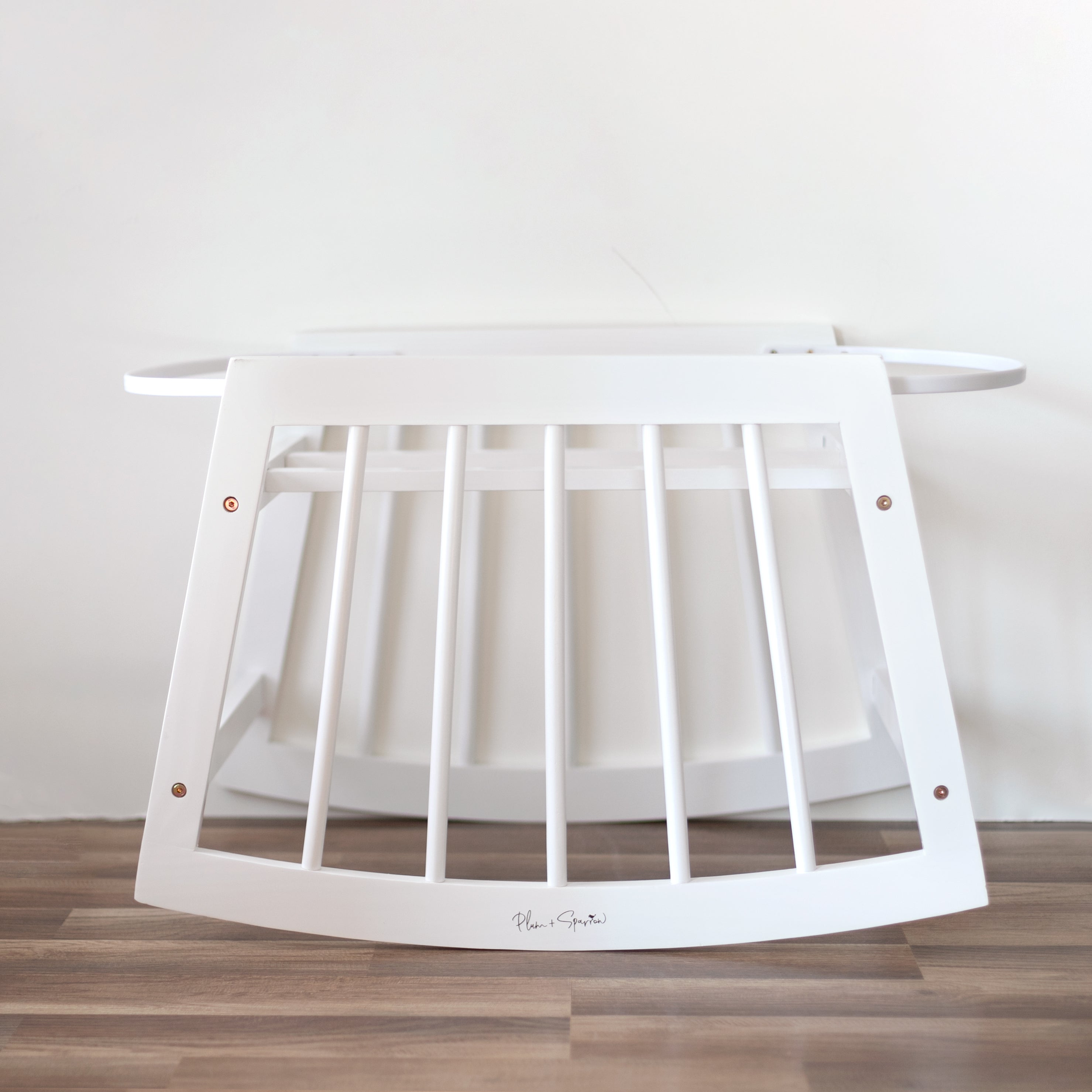 White wooden crib with a mattress on a wooden floor against a white wall