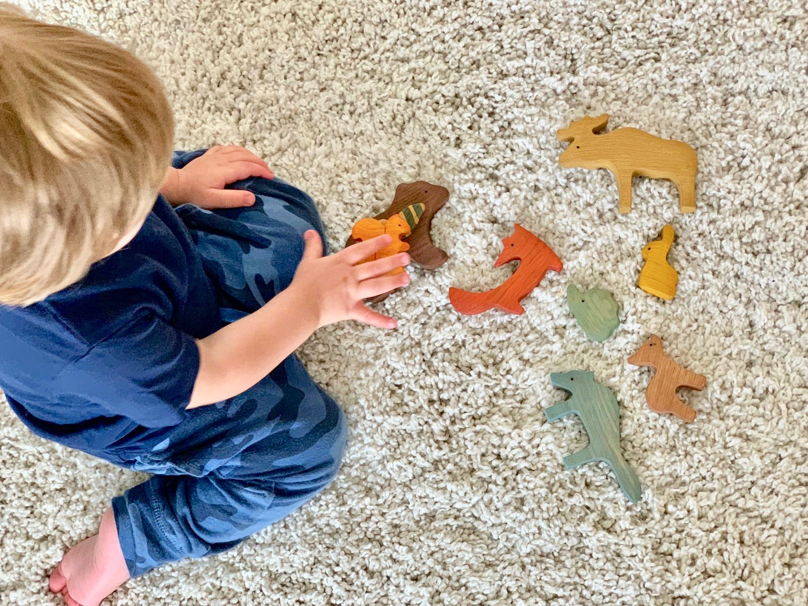 Child playing with wooden animal toys on a carpeted floor