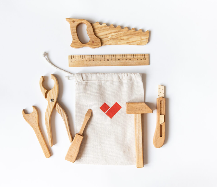Set of wooden tools including a saw, pliers, hammer, and ruler on a white background with a small pouch featuring a red logo.